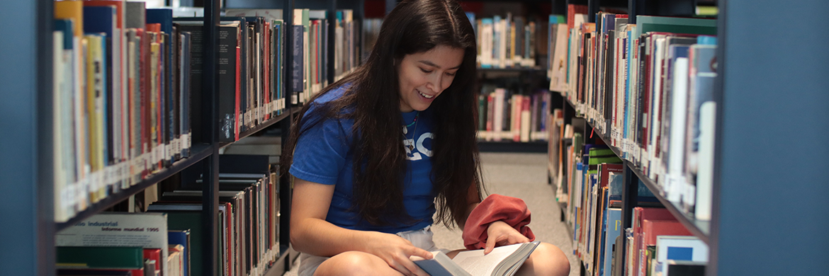 Teen girl reading between bookshelves